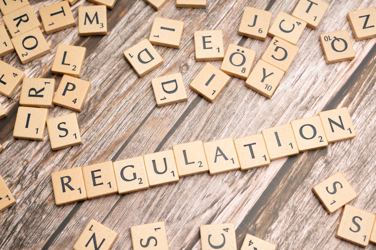Services-01 Wooden letter tiles spelling 'Regulation' on a textured wood background, conveying themes of compliance and structure.