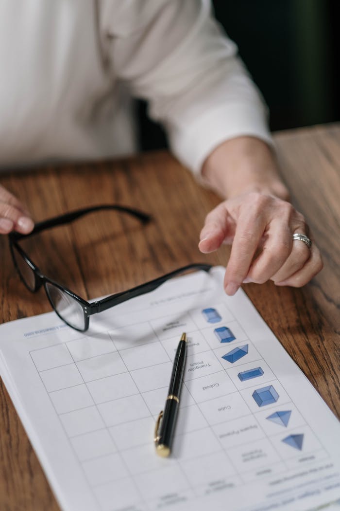 A person reviews paperwork with a pen and glasses on a wooden surface, emphasizing business analysis.